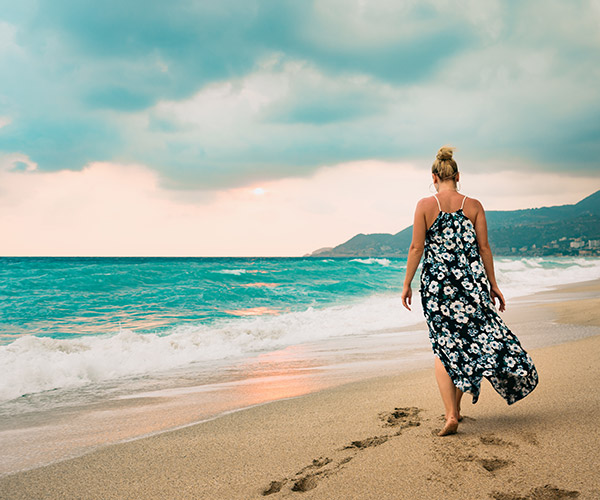 Woman in long dress walking on seashore Woman in long dress walking on seashore