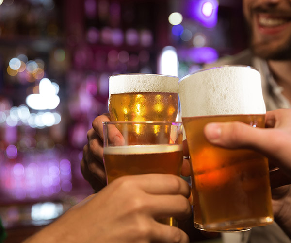 Young men toasting with beer while sitting in pub together Young men toasting with beer while sitting in pub together